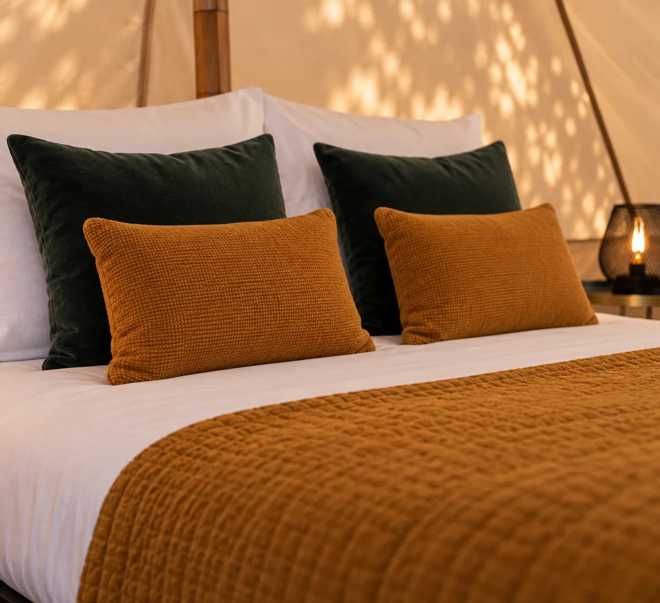 Close-up of green velvet and mustard textured cushions on a white-linen bed inside a Hotel Melody Studio Lounge bell tent.