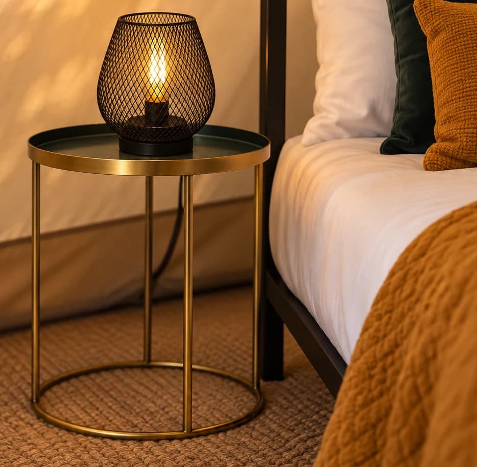 A glowing mesh lantern on a brass side table beside a bed with a mustard throw, inside a Hotel Melody Studio Lounge bell tent.