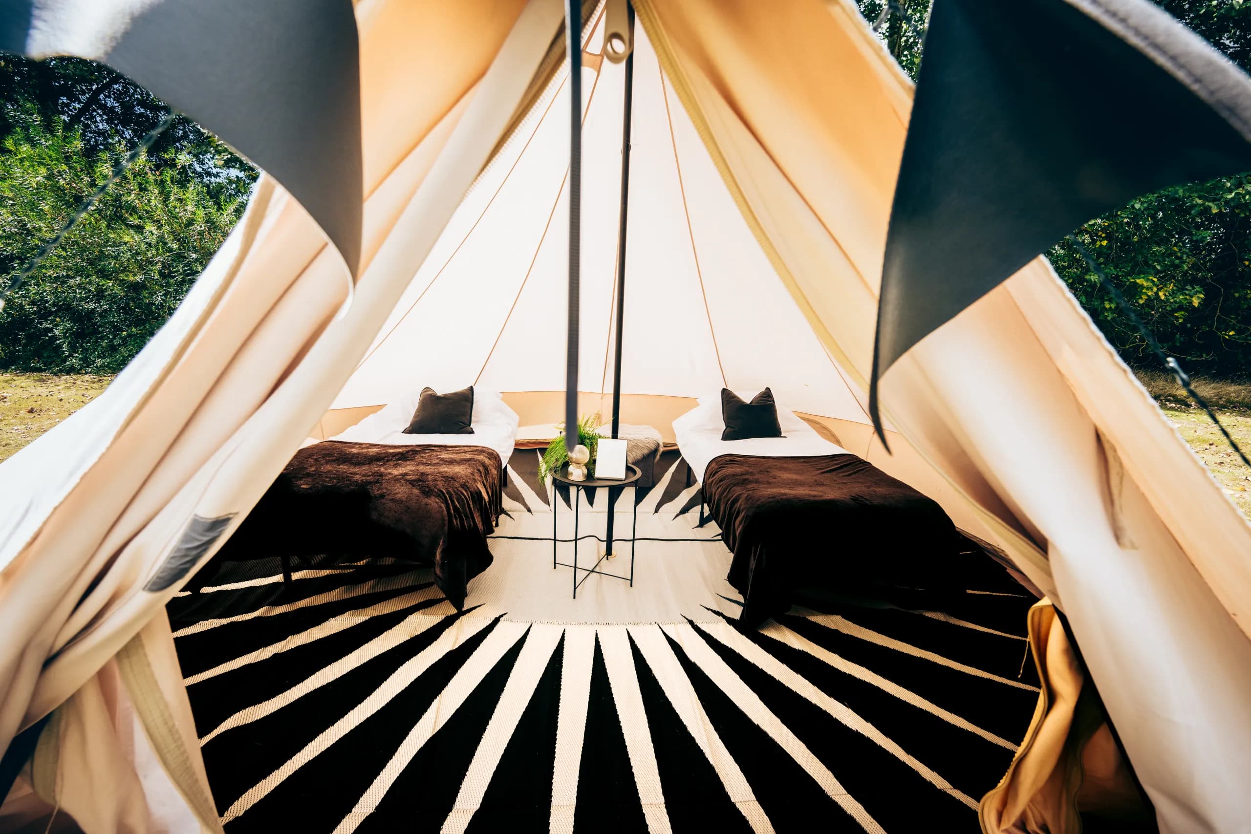 Twin camp beds with brown throws either side of a small side table, seen through the open door of a Hotel Melody Encore Lounge bell tent.